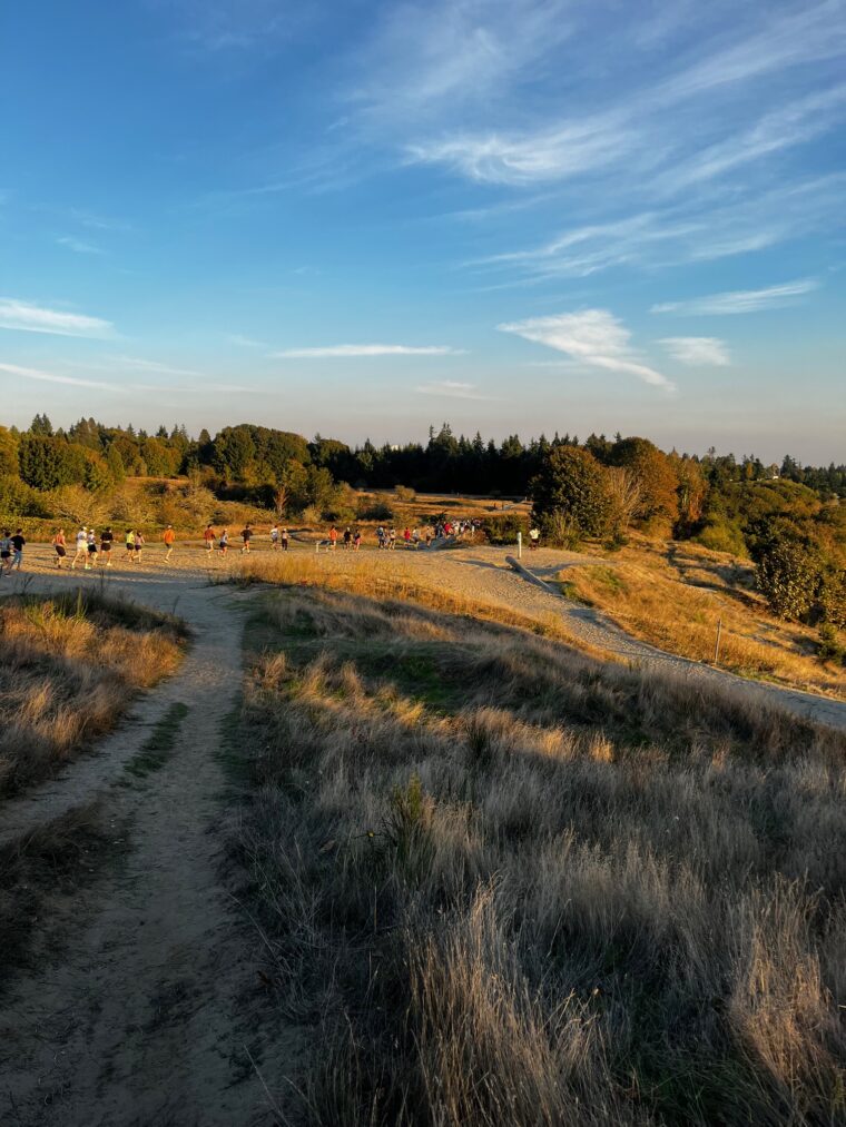 A large group of Team 7 Hills runners from Seven Hills Running Shop Wednesday night group run, Seattle running on a trail in Discovery Park.