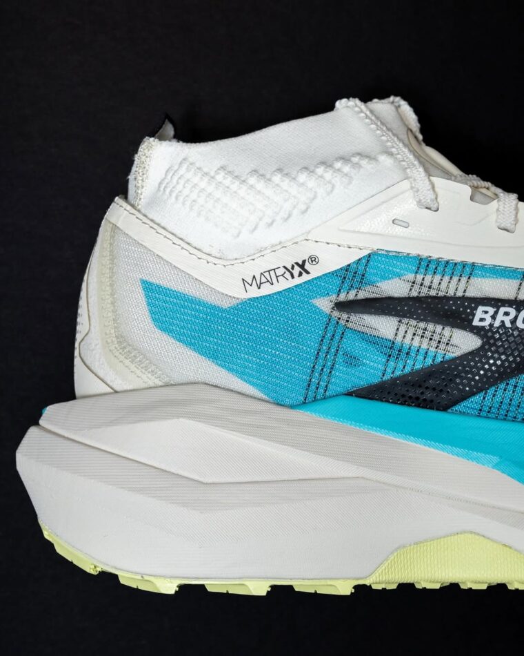 Partial image of the Brooks Cascadia Elite running shoe from the side. The trail shoe is white and has a vivid aqua blue highlight.