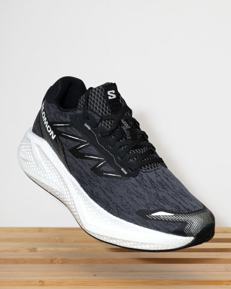 A single right shoe from a pair of black and white Salomon Aero Glide 4 road running shoes. The shoe is angled slightly to the left, showing both the side and top, giving it a sleek, modern look typical of performance running footwear.