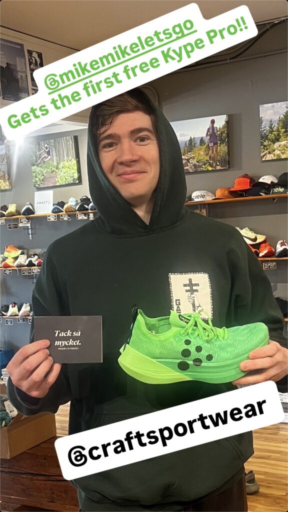 Craft Kype Pro #teamgreen super shoe winner #1 holding up a pair of shoes in front of the wall of shoes at Seven Hills Running Shop.