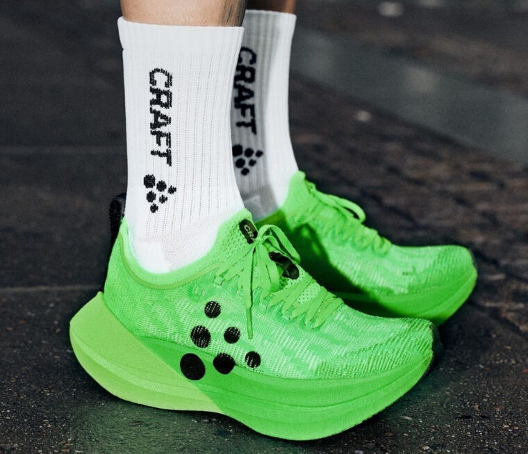 A runner wearing white crew shirts with the words Craft and the Craft brand logo written down the sides and #Teamgreen Kype Pro super shoes.