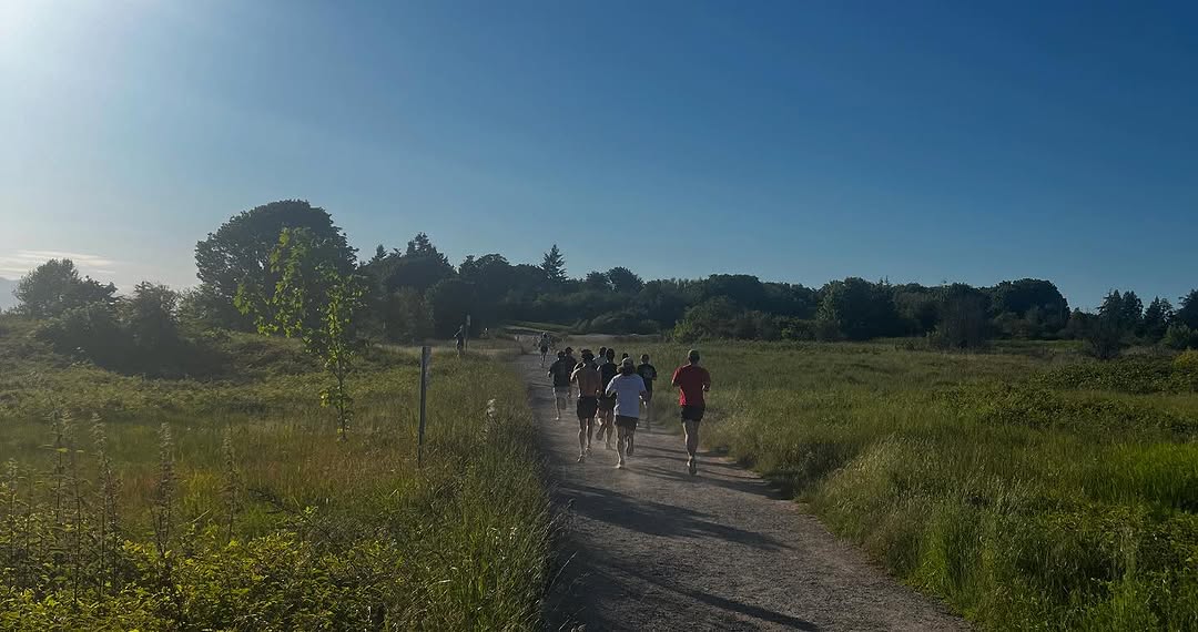 A group of trail runners running along a wide dirt path at Discovery Park, Seattle.
