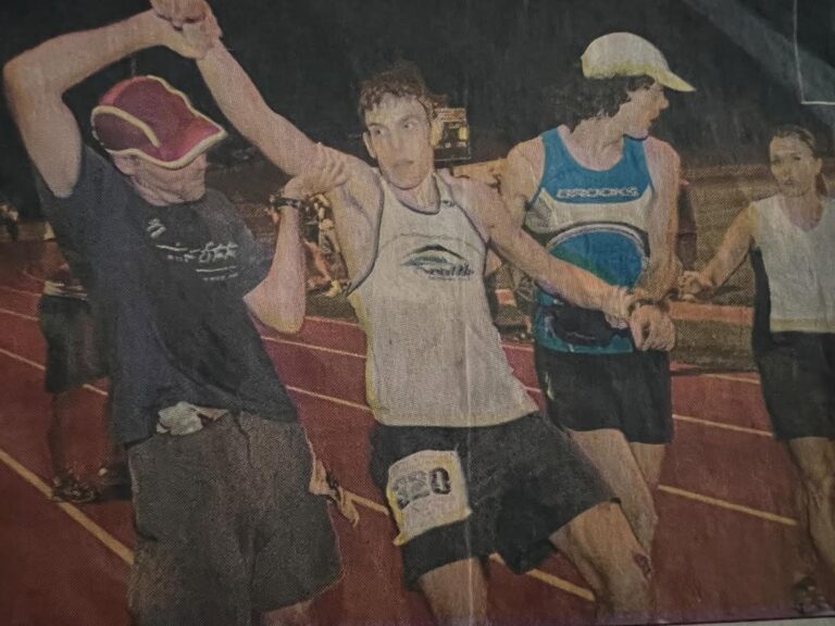 An exhausted runner #320 is helped and partially carried along Placer High track towards the finish line of the WS100 in 2006