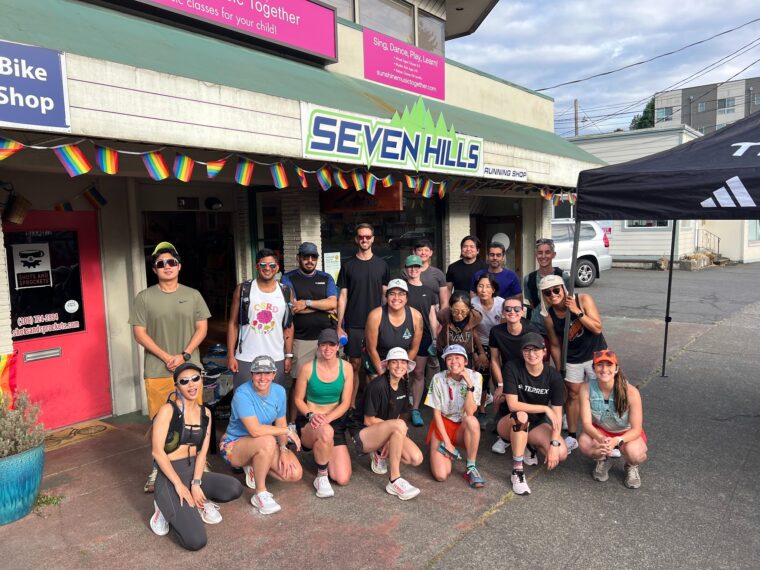 A group of runners lined up and posing for the camera in front of Seven Hills Running Shop